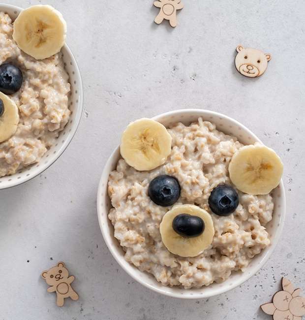 Bowl of oatmeal with slices of banana and blueberries in the shape of a face